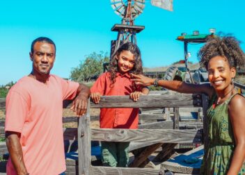 Smiling family of three at the farm, with windmill background.