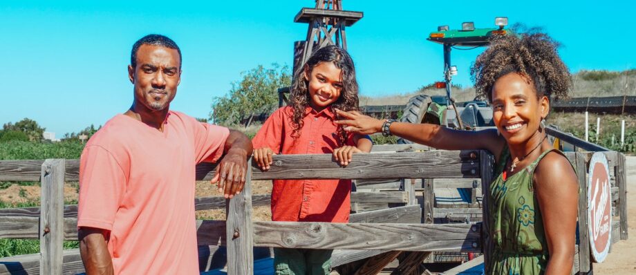Smiling family of three at the farm, with windmill background.