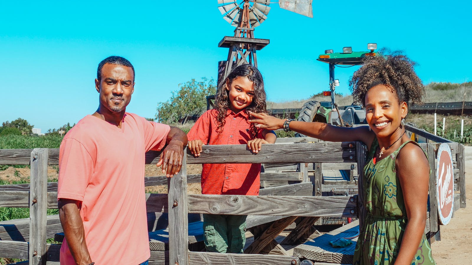 Smiling family of three at the farm, with windmill background.