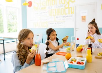 Group of schoolgirls having a break, eating healthy snacks at a canteen table.