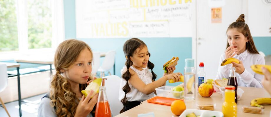 Group of schoolgirls having a break, eating healthy snacks at a canteen table.