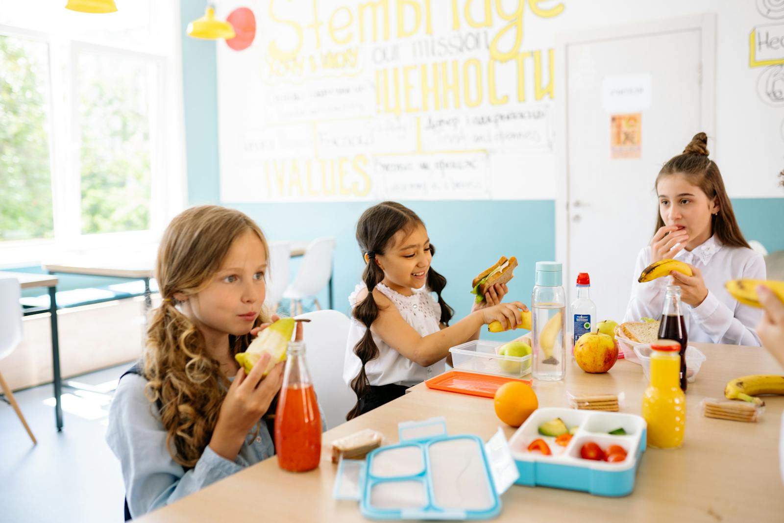 Group of schoolgirls having a break, eating healthy snacks at a canteen table.